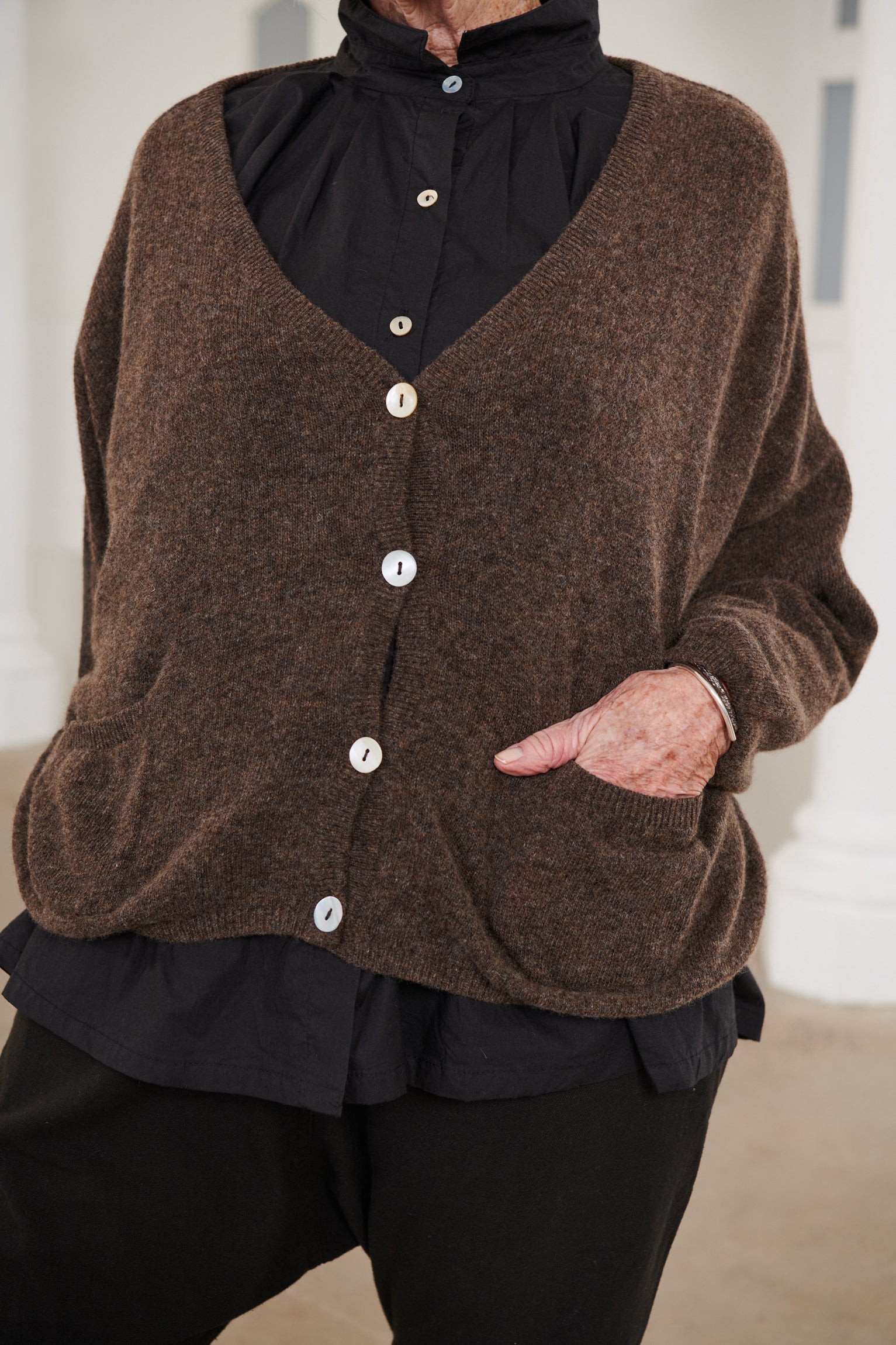 A MegbyDesign model is wearing a brown oversized wool cardigan with two pockets and buttons at the front