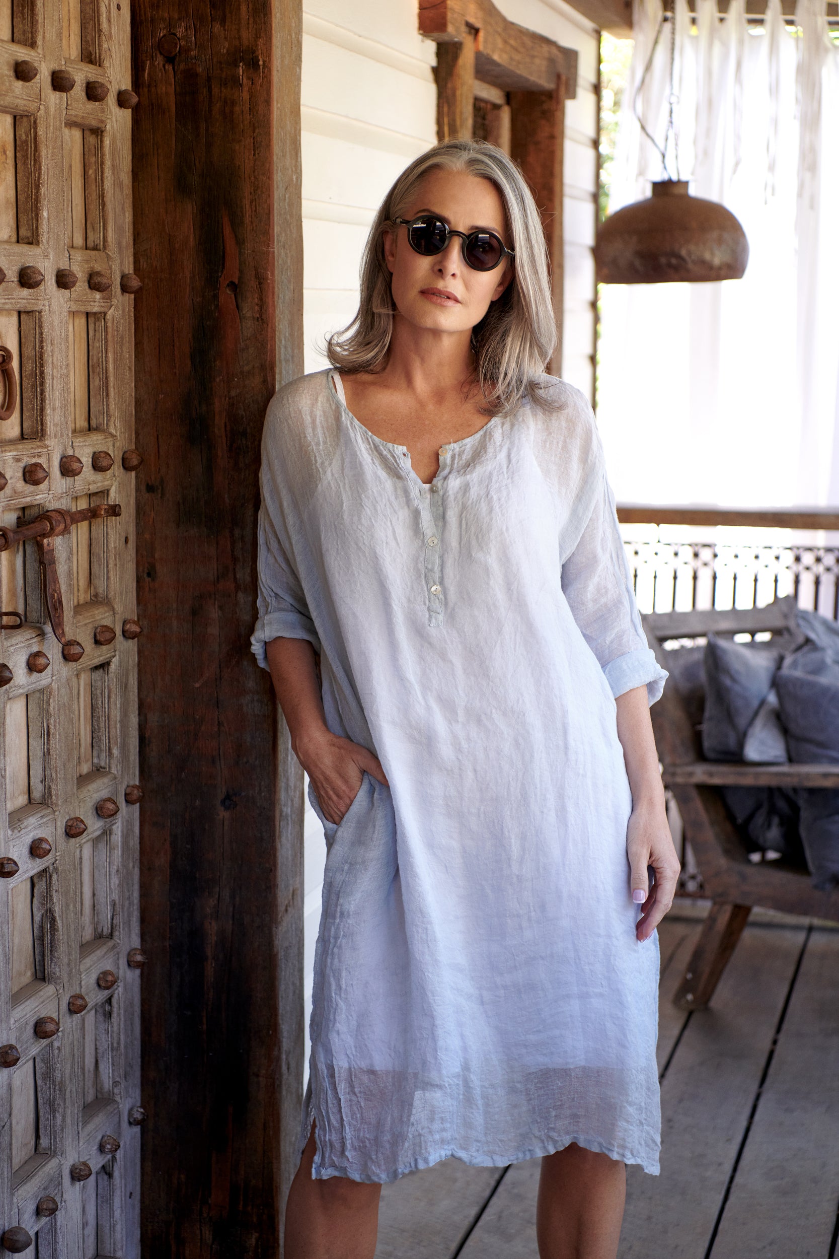 A MegbyDesign model is wearing a mid length white linen dress in white which features side pockets and double stitching