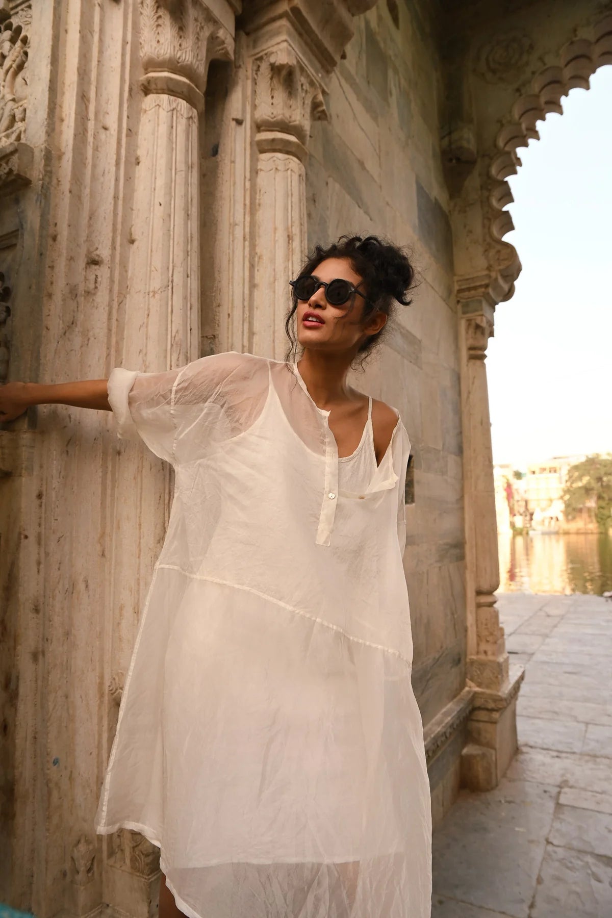 Woman in MegbyDesign black silk organza dress and silk organza top poses by a stone wall in an old European town.
