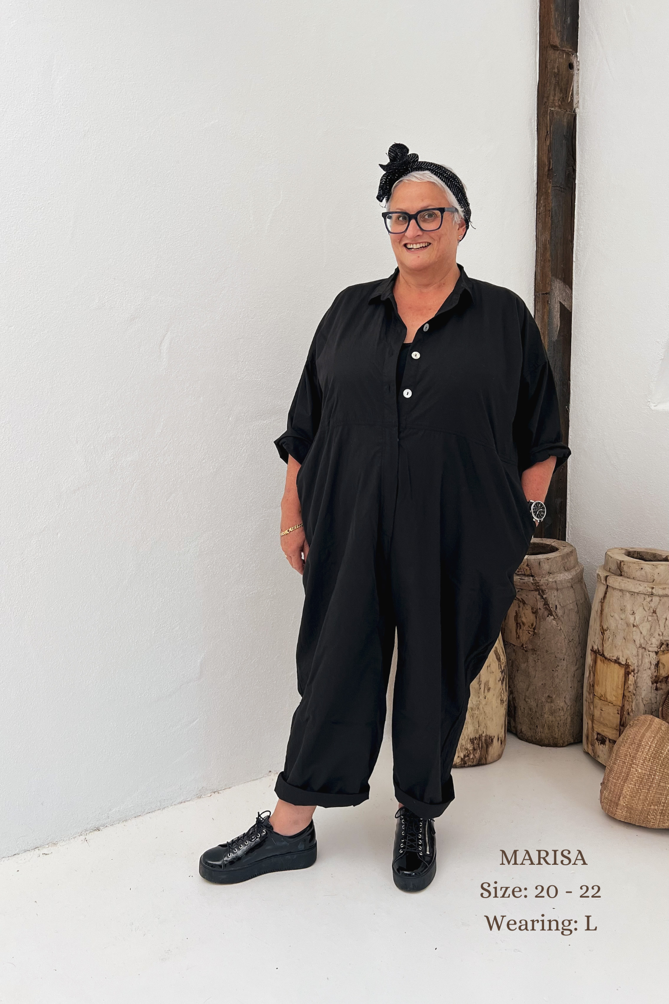 A MegbyDesign model is wearing a black boiler suit made from cotton twill with side and back pockets, double stitched and agoya shell buttons.