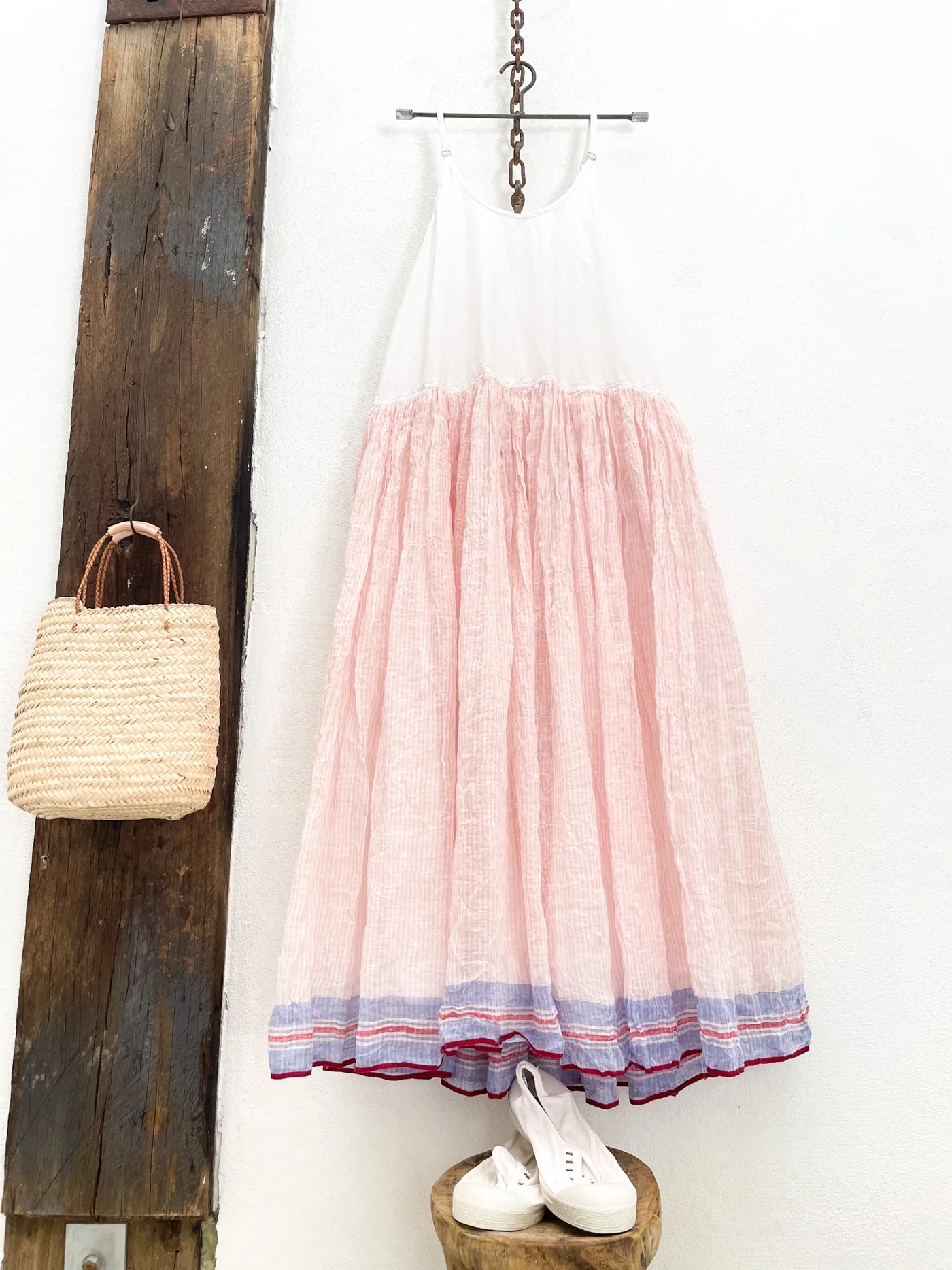A MegbyDesign white, pink and purple dress hanging on a white wall paired with accessories