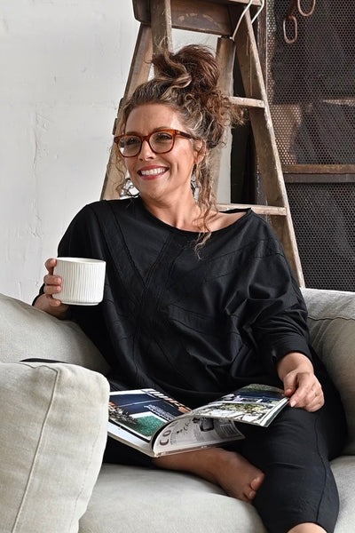 Woman dressed in a black cotton loungewear set reading a magazine on the couch.