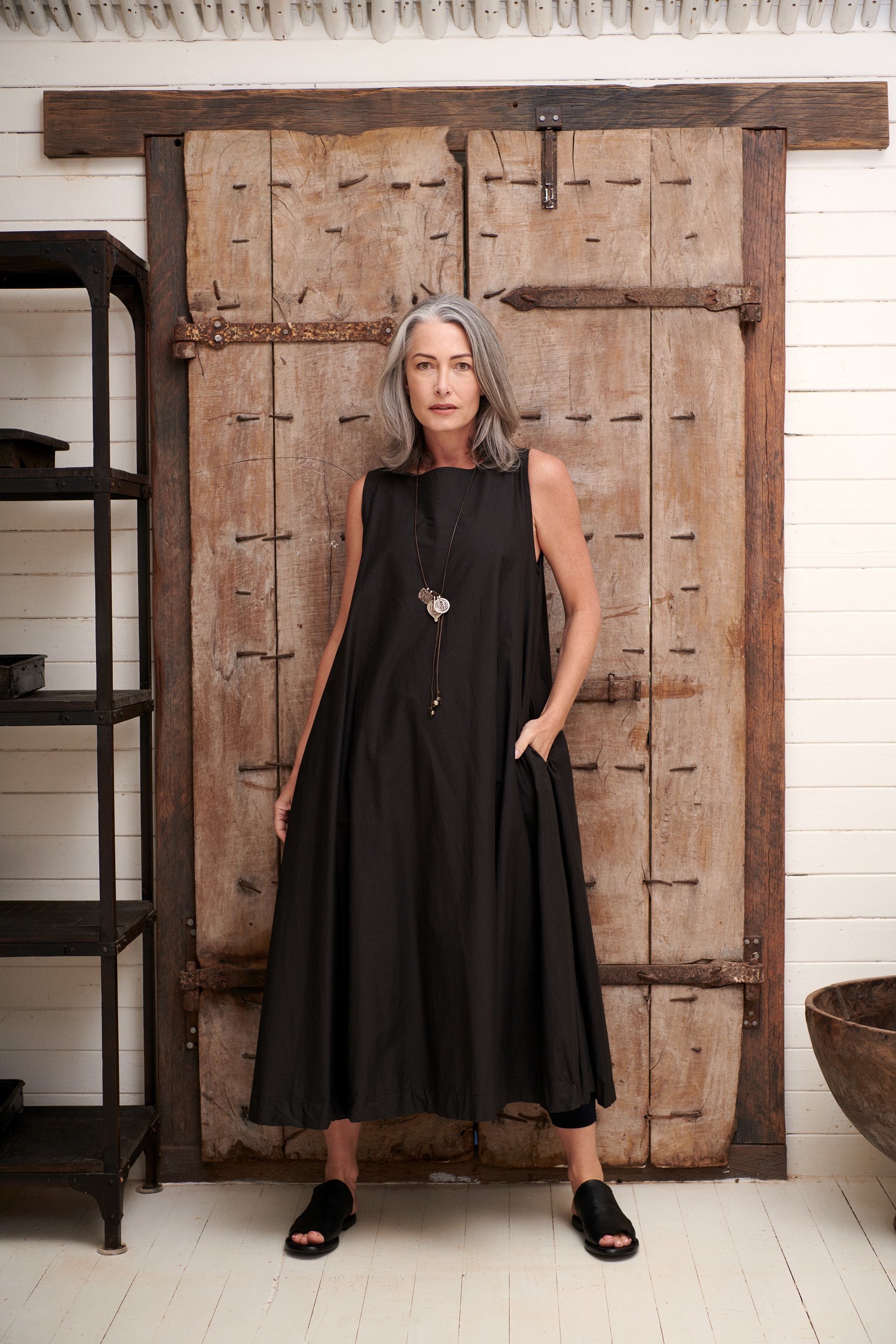 A MegbyDesign model is wearing a long, black, sleeveless, fully lined dress which features a flattering high neckline and side pockets. 