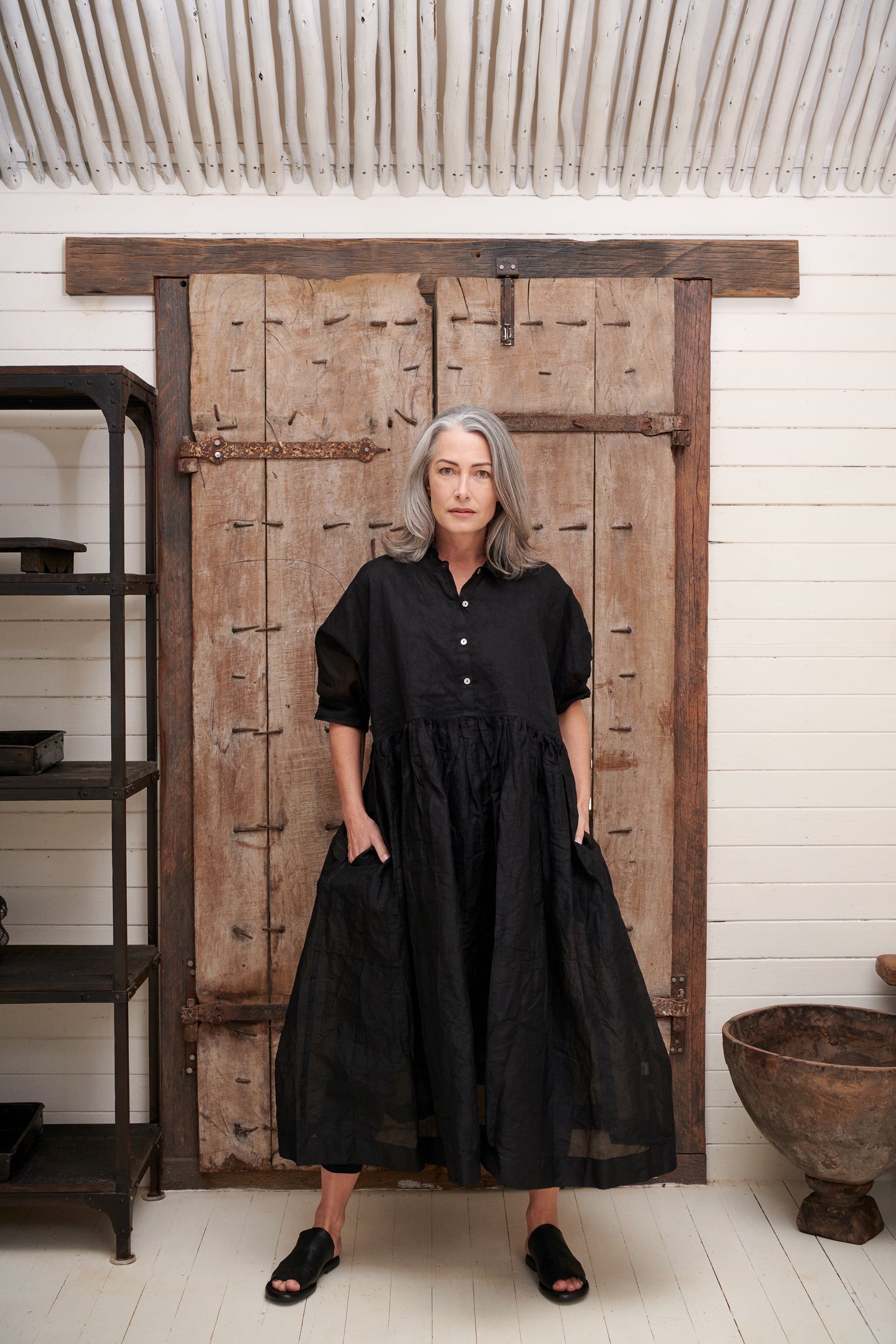 A MegbyDesign model is wearing a long black dress with side pockets, double stitching and a tiny collar to accent and give detail to the bodice.
