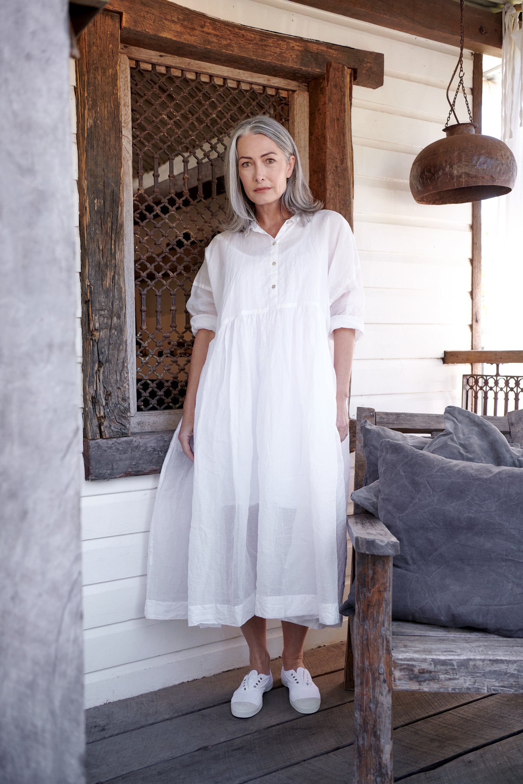 A MegbyDesign model is wearing a long white cotton dress with a collared neck and rolled sleeves