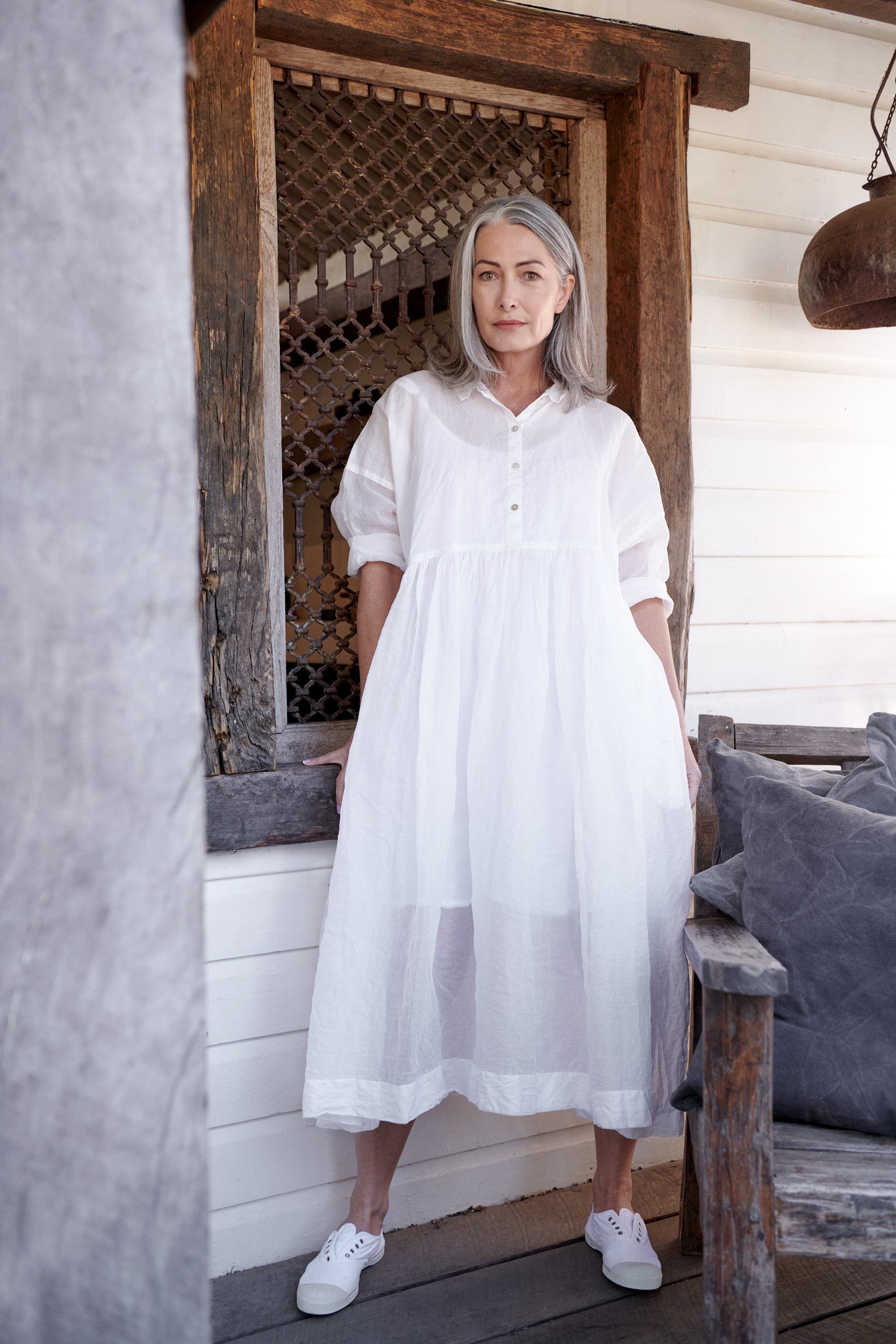 A MegbyDesign model is wearing a long white cotton dress with a collared neck and rolled sleeves