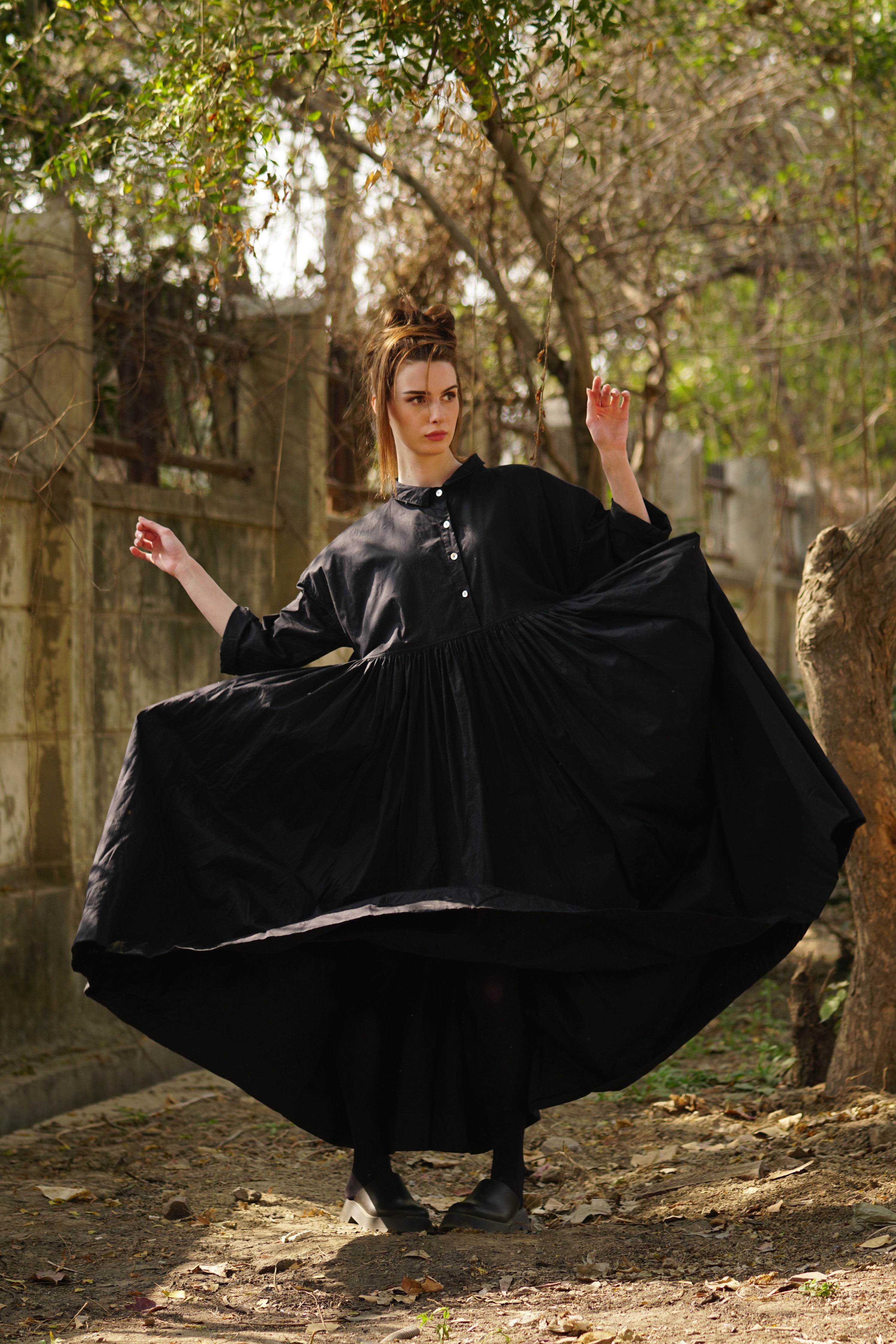 A MegbyDesign model is wearing a long, black, dress with side pockets, double stitching and a tiny collar