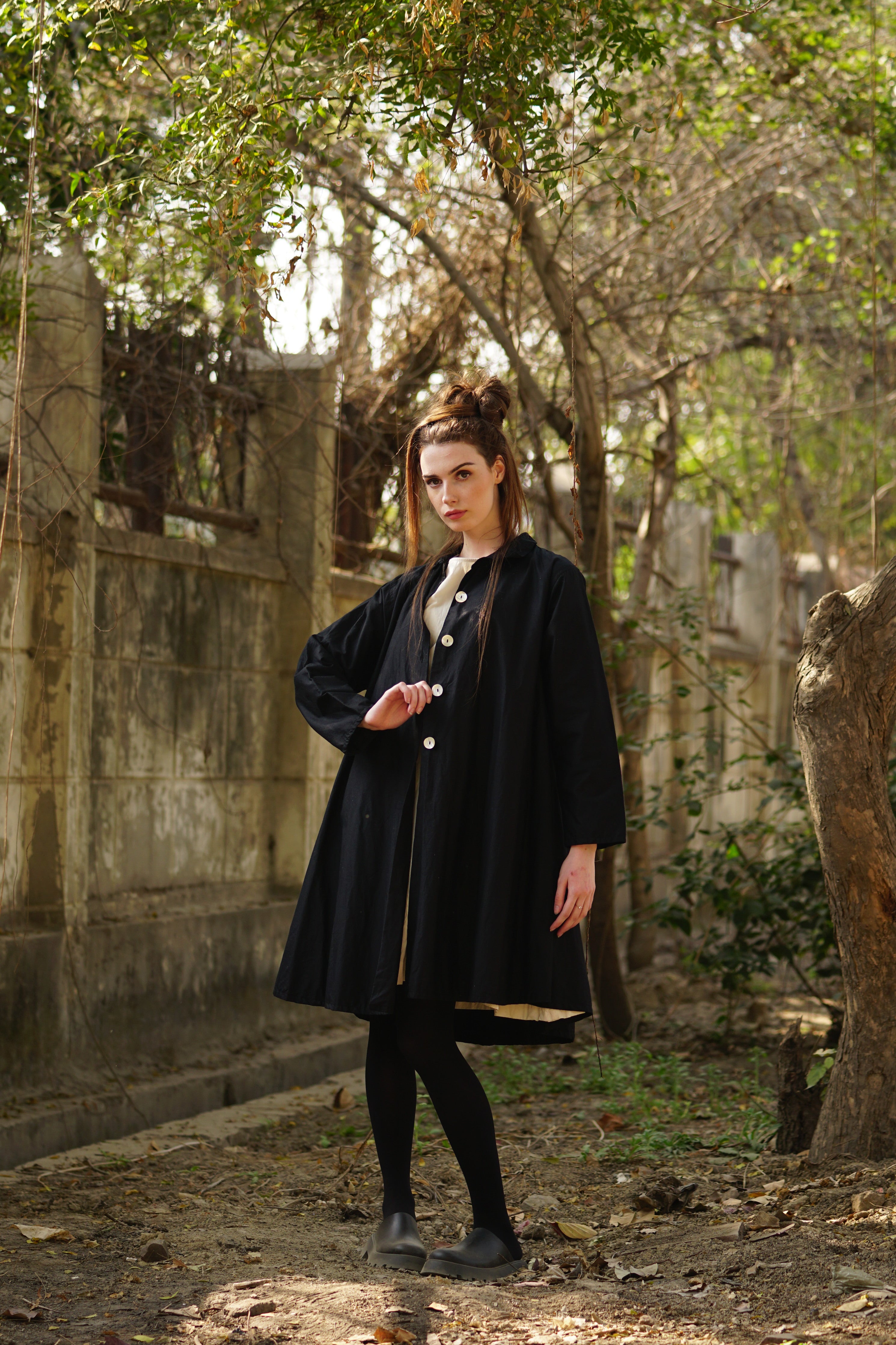 A MegbyDesign model is wearing a lined cotton twill black coat with large black spots featuring agoya shell buttons, side pockets and a classic cut collar
